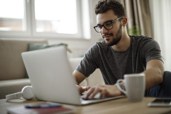 man with glasses works on laptop computer with white mug on the side