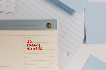 Notebook papers, sticky notes, and a planner on top. The planner has a section titled "To do list." In red sharpie written underneath says "SO MANY THINGS"