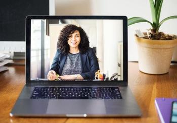 Laptop on desk, screen showing a woman wearing professional attire.