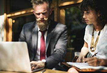 Image of man and woman in professional attire looking at laptop.