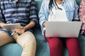 People sitting on couch in a row on laptops and writing in notebooks.