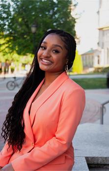 Cydni Young wearing an orange dress, while smiling and sitting on a bench 